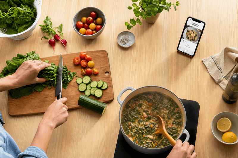 Hands chopping vegetables and stirring a pot, with a phone propped up nearby, untouched